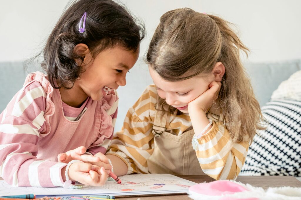 Two girls sharing a happy moment indoors, drawing and laughing together.